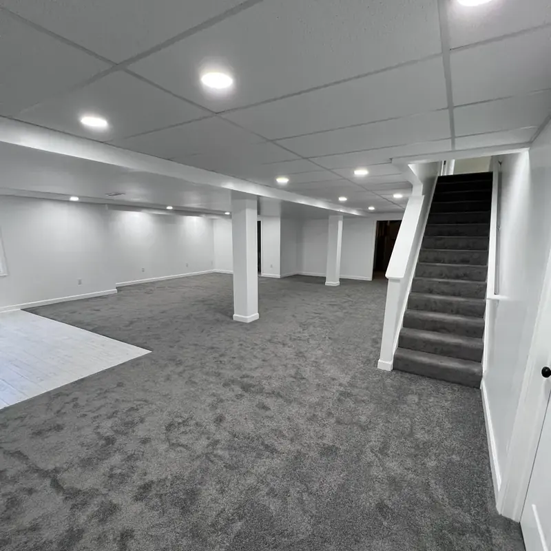 Finished basement with gray carpet, drop ceiling, staircase