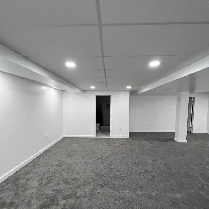 Empty finished basement room with bathroom doorway visible