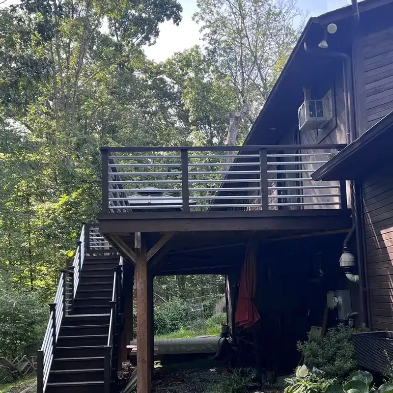 Elevated dark deck with stairs, wooded backyard view
