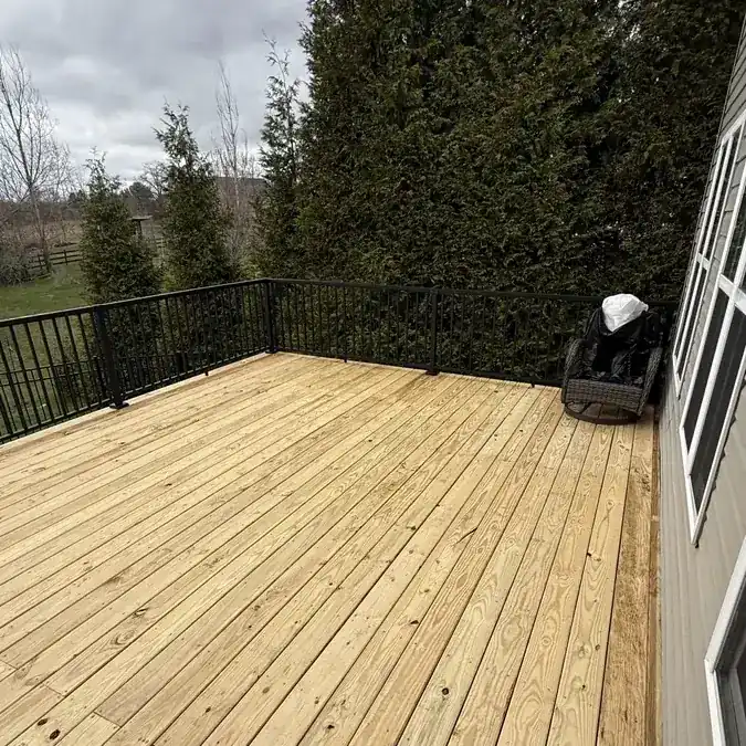 Empty wood plank deck with black railings overlooking yard