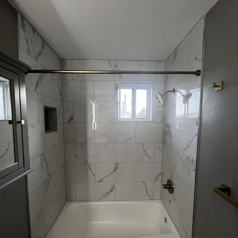 Tub shower with marble tile niche and gold rod
