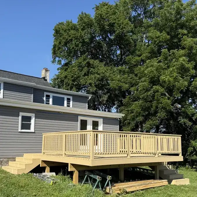 New wood deck construction with railings behind a gray-sided home